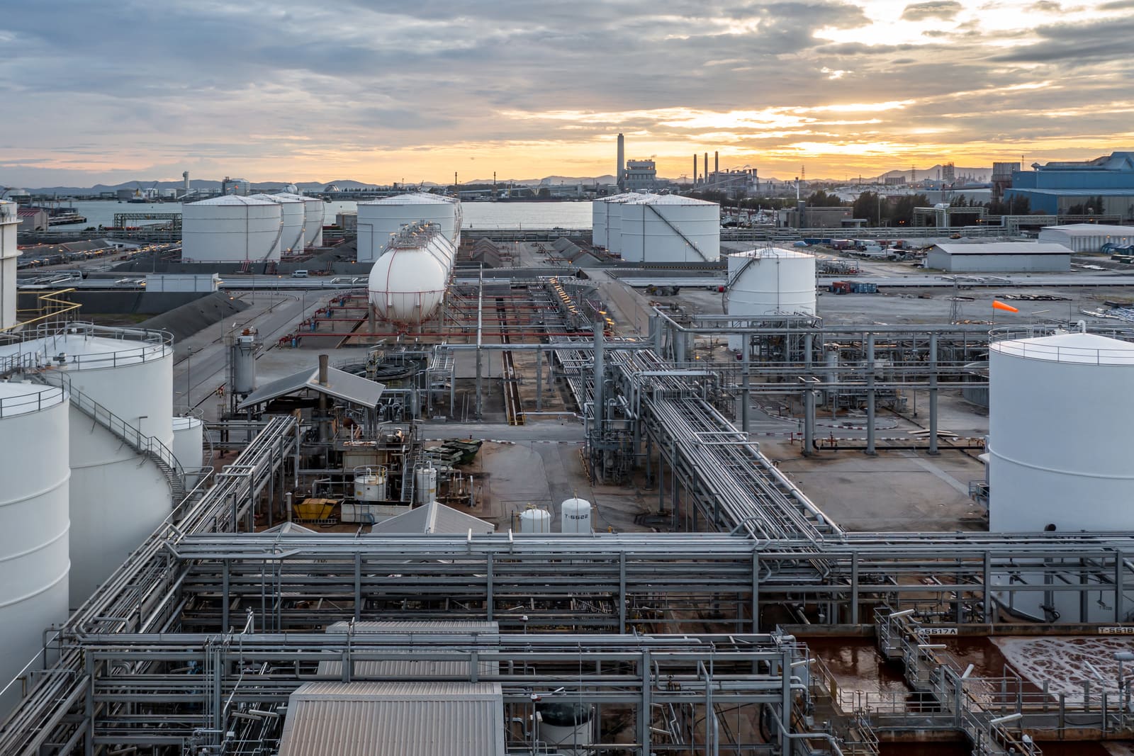 A petroleum tank farm at dusk, with storage tanks and pipe runs across the site